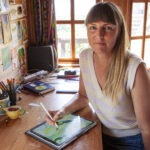 Portrait of Rebecca ter Borg. She is a Pakehā-presenting woman with long fair hair and a fringe. She is seated with an iPad and pen and is facing the camera